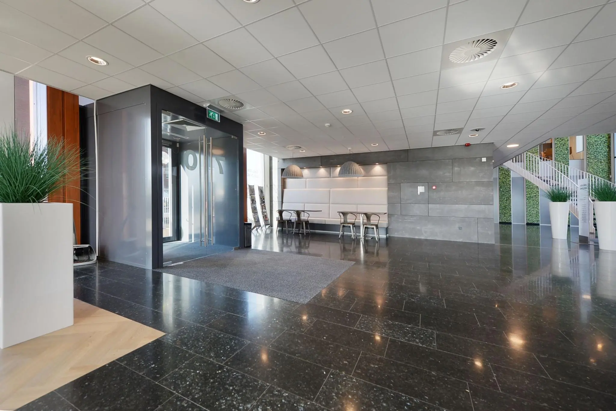 Moderne ontvangsthal van een kantoorpand aan de Laan van Zuid Hoorn met zithoek, glazen entree en trap naar boven.